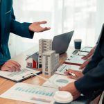 Conseillers en gestion de patrimoine présentant des stratégies d’investissement immobilier et financier autour d’une maquette de bâtiments