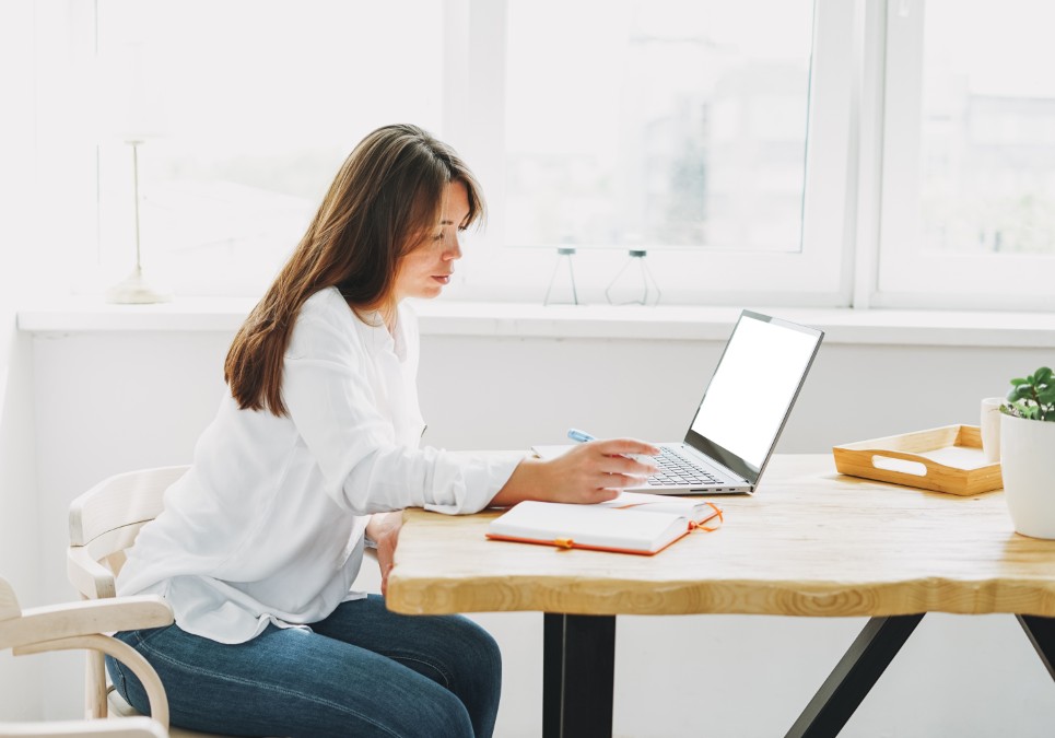 Femme adulte prenant des notes devant son ordinateur lors d'une formation à distance en comptabilité.